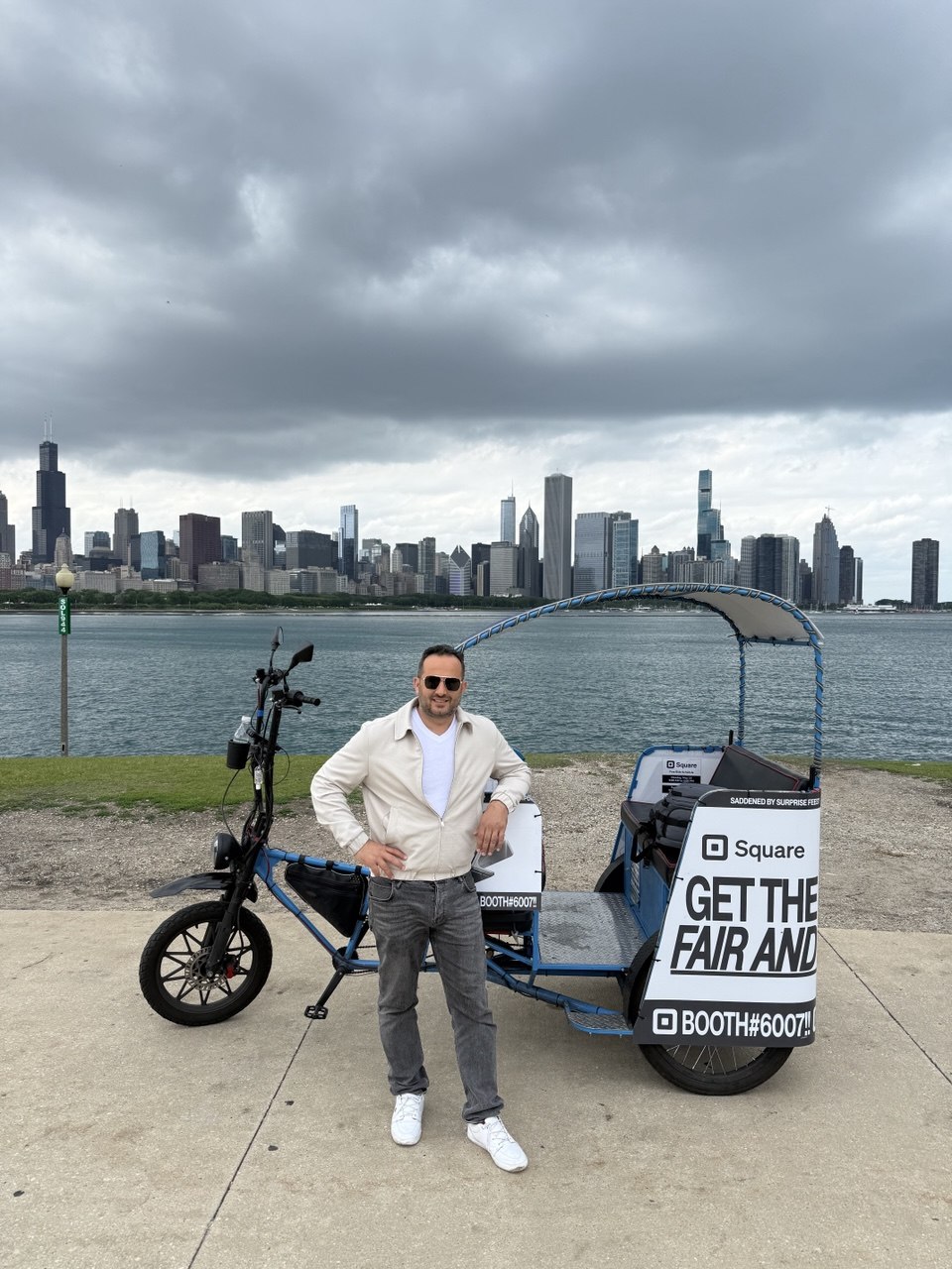 Ali Horuz beside a Square-branded electric pedicab with the Chicago skyline behind